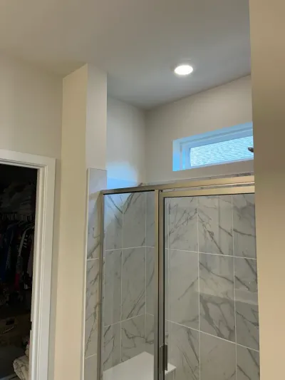 A tiled walk-in shower with a glass door, marble-look tile, and a small window above it.