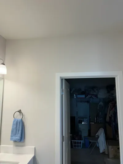 Bathroom wall with a towel ring and sconce light beside an open door into a cluttered closet.