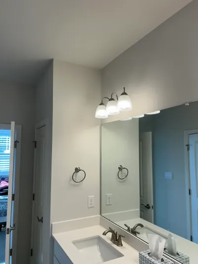 Bathroom vanity with a large mirror, brushed nickel fixtures, and a three-light fixture above.