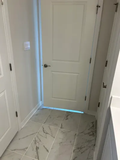 Finished bathroom hallway with diagonal marble tile flooring and a white paneled door.