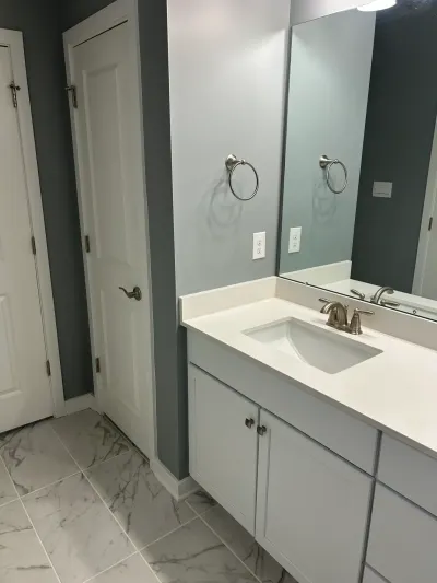 A finished bathroom vanity with white quartz counter, brushed nickel fixtures, and marble-look tile flooring.