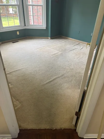 Empty bedroom with worn carpet and teal walls, viewed from the doorway before renovation.