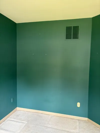 Corner of an empty room with dark teal walls, cream ceiling, worn carpet, and a wall vent.