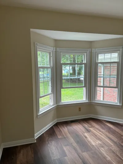 Empty living room corner with a bay window and dark wood-look flooring.