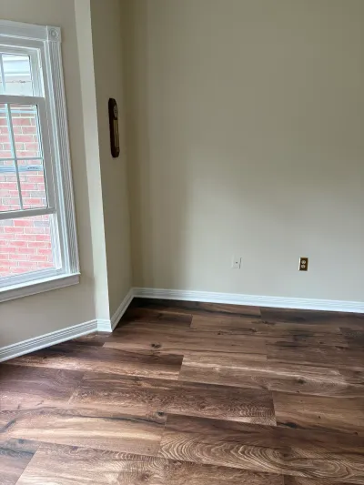Empty room with new dark wood-look vinyl plank flooring and a window showing brick exterior.