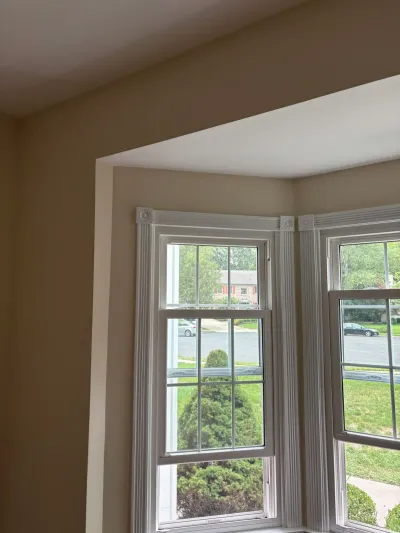 A bay window corner with detailed fluted trim, framed by tan walls and looking out onto a residential street.