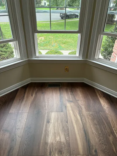 A bay window nook with new wood-look flooring and white trim overlooking a front yard.