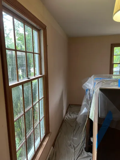 Hallway with wood-framed windows and furniture covered in plastic during a home renovation.