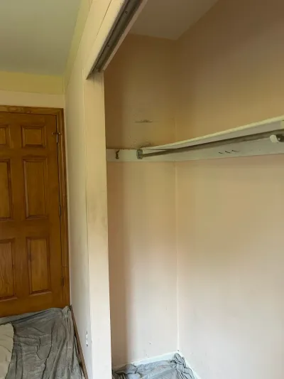 Empty closet before renovation with a dusty shelf, exposed sliding door track, and no doors installed.