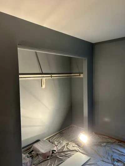 A closet alcove mid-renovation with freshly painted dark gray walls and a work light on the floor.