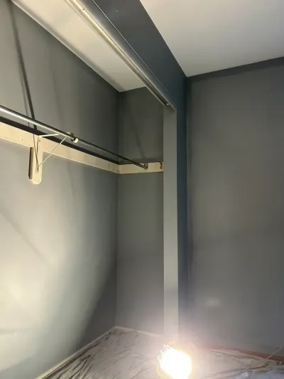 A closet mid-renovation with newly painted dark gray walls, an old closet rod, and a work light on the floor.