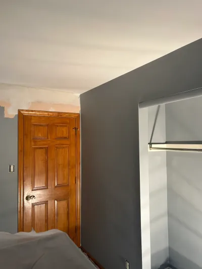 A bedroom mid-paint job with a gray accent wall, an open closet, and a wood-paneled door in the background.
