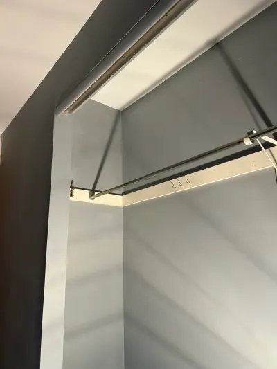 Upward view inside a gray-painted closet showing a metal hanging rod mounted in the corner.
