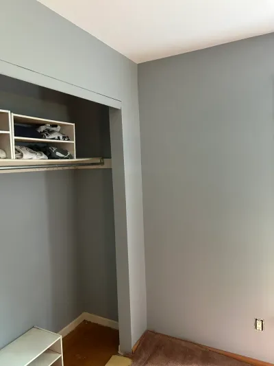 A bedroom closet with gray walls, a single rod, and a small shelving unit before renovation.