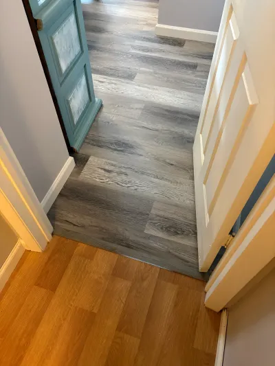 Hallway showing a flooring transition from oak laminate to new gray wood-look vinyl plank flooring.