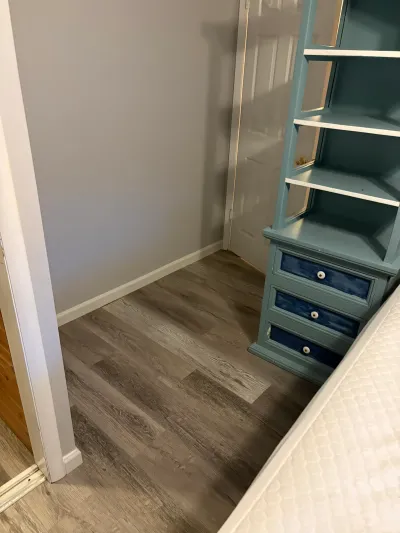 Bedroom corner with grey flooring, teal shelving unit with navy drawers, and a mattress nearby.