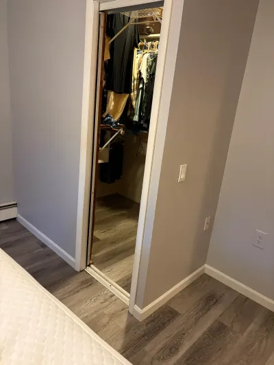 Hallway view of a partially open closet door showing wire shelving and hanging clothes.