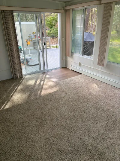 A living room mid-renovation with carpet transitioning to plank flooring near a sliding glass door leading to a deck.