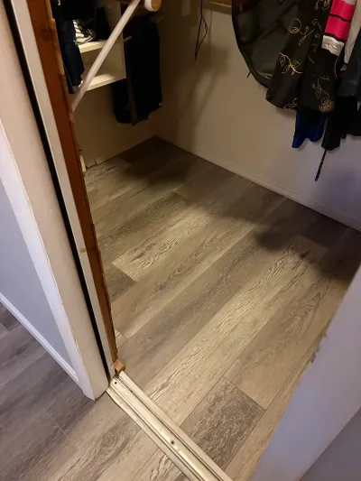 A walk-in closet with new grey wood-look vinyl plank flooring and an unfinished door threshold mid-renovation.