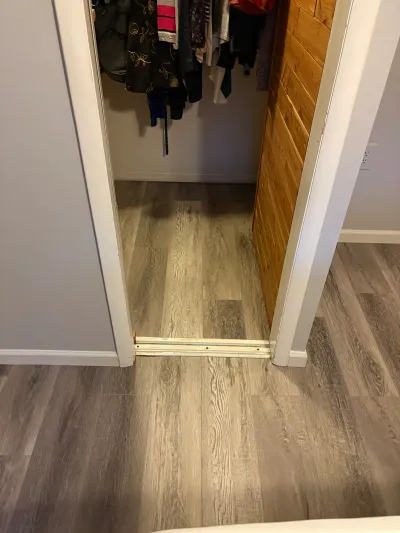 A closet doorway with new grey wood-look vinyl plank flooring and a metal threshold strip.