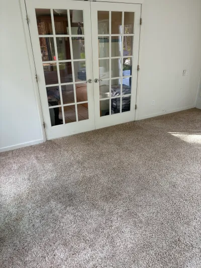 Empty carpeted room with stained flooring and French glass doors leading to a tiled adjacent space.