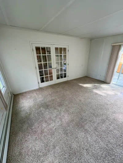 Empty carpeted living room with french doors and a sliding glass door leading to a deck.