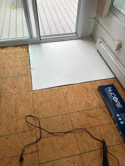 Subfloor prepped with chalk lines near a sliding door, with a box of vinyl flooring staged for installation.