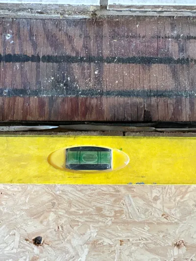 A yellow level with a bubble vial held against weathered wood shingle siding during exterior work.
