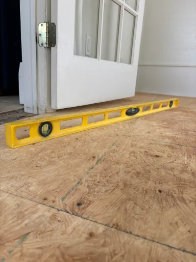 A yellow level rests on OSB subfloor near an open French door during a renovation.