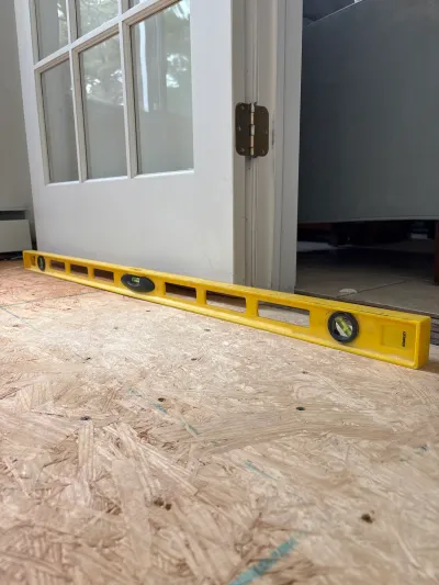 A yellow level rests on an exposed OSB subfloor near an open French door during renovation.