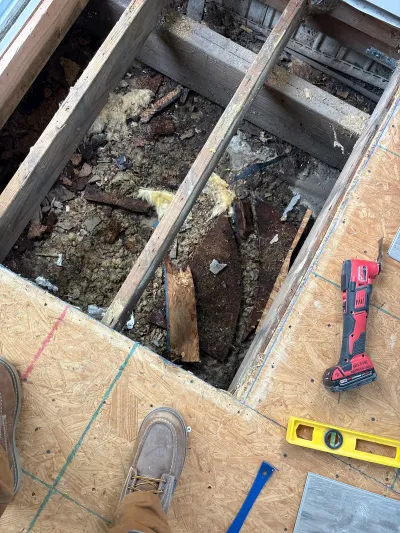 Overhead view into an open subfloor cavity showing joists, insulation, and debris during a floor repair.