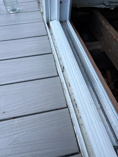 Close-up of a dirty sliding door track meeting composite decking, with framing visible below.