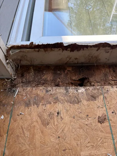 Close-up of a rotted window sill with exposed decayed wood and water-damaged OSB sheathing.