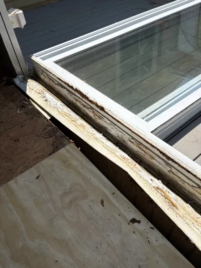 Close-up of rotted window sill trim being replaced with new plywood during exterior repair work.