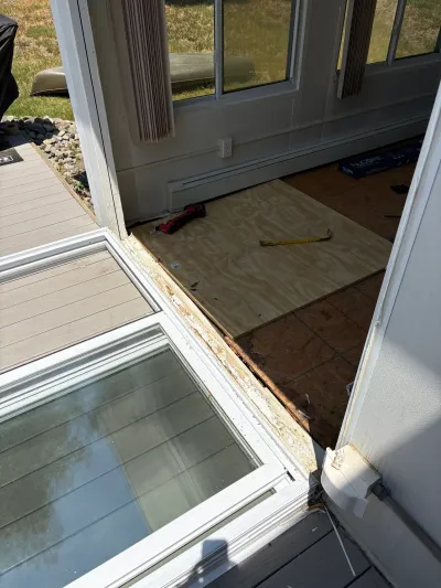 Sunroom doorway mid-repair with exposed water-damaged subfloor, plywood patch, and tools on the floor.