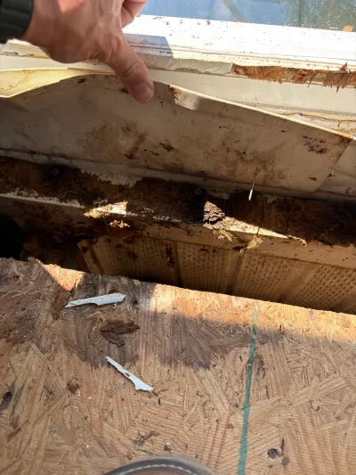 Close-up of a damaged, rotted roof edge with a hand pointing to the deteriorated section.