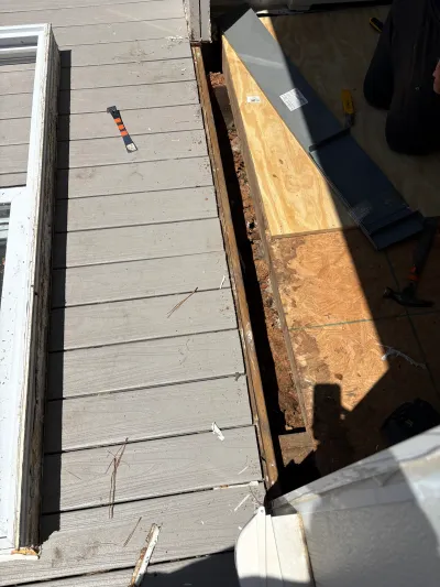 Deck boards pulled back to expose plywood subfloor and flashing during a repair near a window.