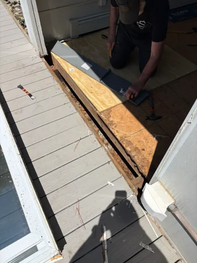 Worker installs a metal threshold piece at a deck doorway during a repair, with subfloor exposed.