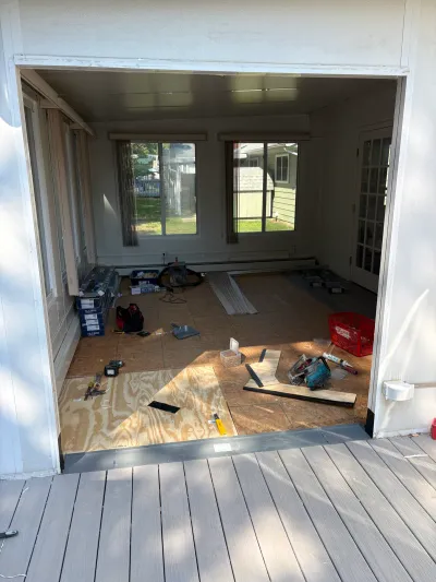 A sunroom under construction with plywood subfloor, partial tile flooring, and tools scattered about.