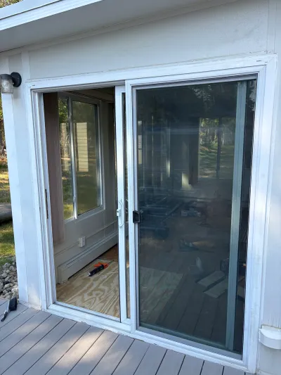 A newly installed sliding glass door on a deck, with an unfinished interior visible through the glass.