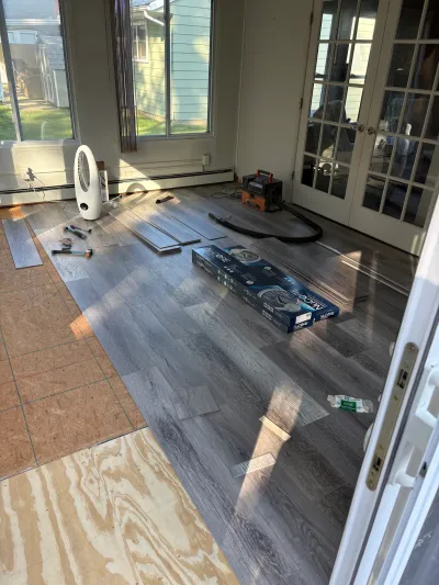 Sunroom floor mid-installation with grey vinyl plank flooring laid over plywood subfloor and tools scattered about.