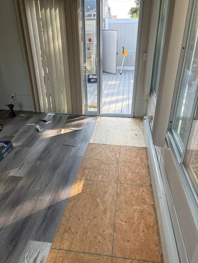 Vinyl plank flooring being installed over OSB subfloor near a sliding door to an outdoor deck.