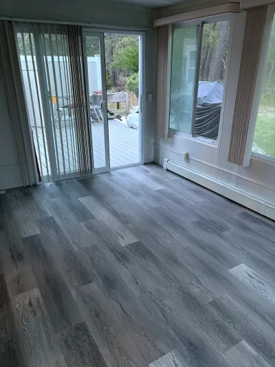 A finished sunroom with grey vinyl plank flooring and sliding glass doors leading to a deck.