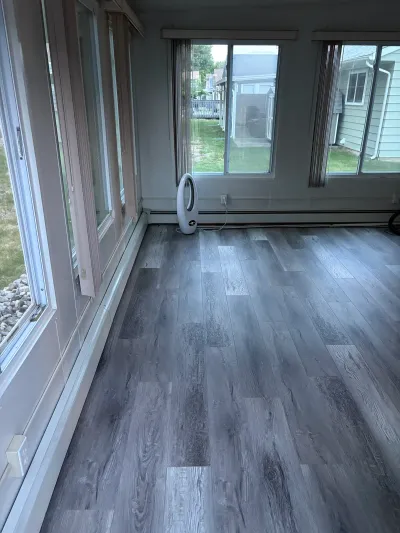 A bright sunroom with gray plank flooring and large windows overlooking a backyard.