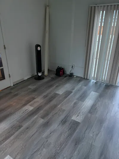 A room with newly installed grey wood-look vinyl plank flooring and tools left near a sliding glass door.