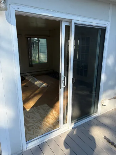 Open sliding glass door reveals a sunroom with exposed plywood subfloor mid-renovation.