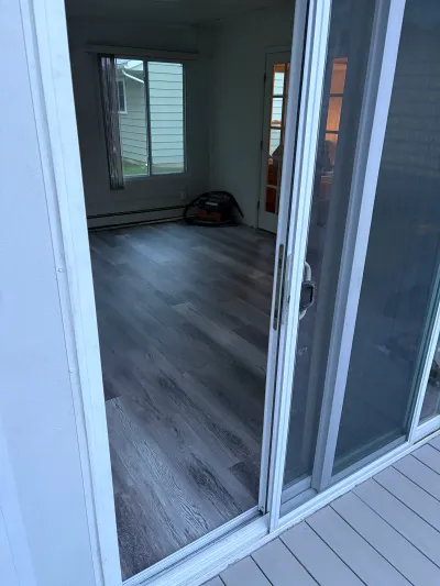 View from a deck through a sliding glass door into a room with new grey plank flooring.