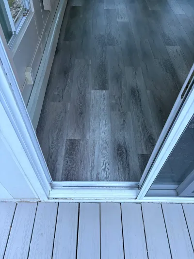 View through an open sliding glass door showing gray plank flooring inside and a composite deck outside.