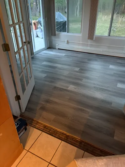 Sunroom with newly installed grey plank flooring, French doors, and view of the backyard.