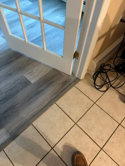 Doorway showing a transition from grey vinyl plank flooring to beige ceramic tile near a baseboard heater.